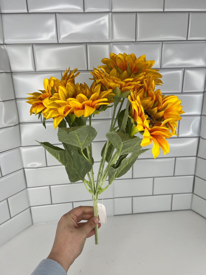 May include: A bouquet of artificial sunflowers with green leaves. The sunflowers are yellow with brown centers.