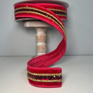 May include: Red velvet ribbon with gold trim and red rhinestone accents. The ribbon is wrapped around a spool.