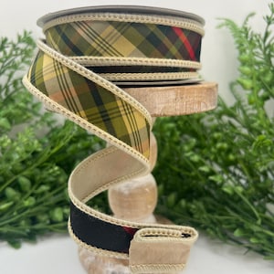 May include: A spool of wired ribbon featuring a plaid pattern in shades of olive green, yellow, black, and red. The ribbon has a light beige stitched edge along both sides and is coiled to display the fabric texture and the multi-colored design.
