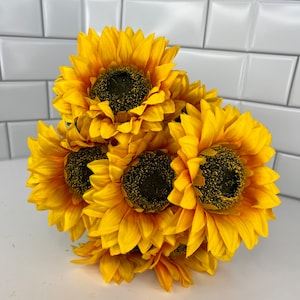 May include: A bouquet of six artificial sunflowers with yellow petals and dark brown centers. The sunflowers are arranged in a cluster, with the petals overlapping.