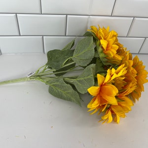 May include: A bouquet of artificial sunflowers with green leaves. The sunflowers are yellow with brown centers.