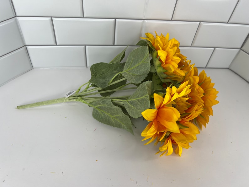 May include: A bouquet of artificial sunflowers with green leaves. The sunflowers are yellow with brown centers.