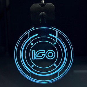May include: A blue LED illuminated keyring featuring the word "ISO" in a futuristic font. The circular design has concentric rings, and a black top section with a small button. The design has a sci-fi aesthetic.
