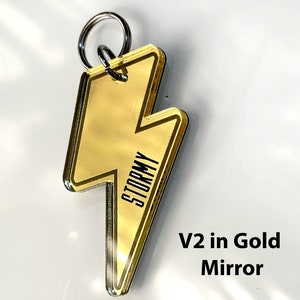May include: Gold lightning bolt keychain with the word "Stormy" printed on it. V2 in Gold Mirror.