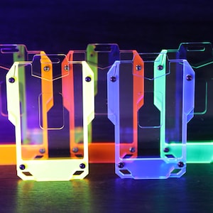 May include: A collection of five rectangular badge holders made of translucent acrylic in neon orange, yellow, red, blue, and green. Each holder features a central cutout, a top slot for a lanyard, and four small black screws securing the frame.