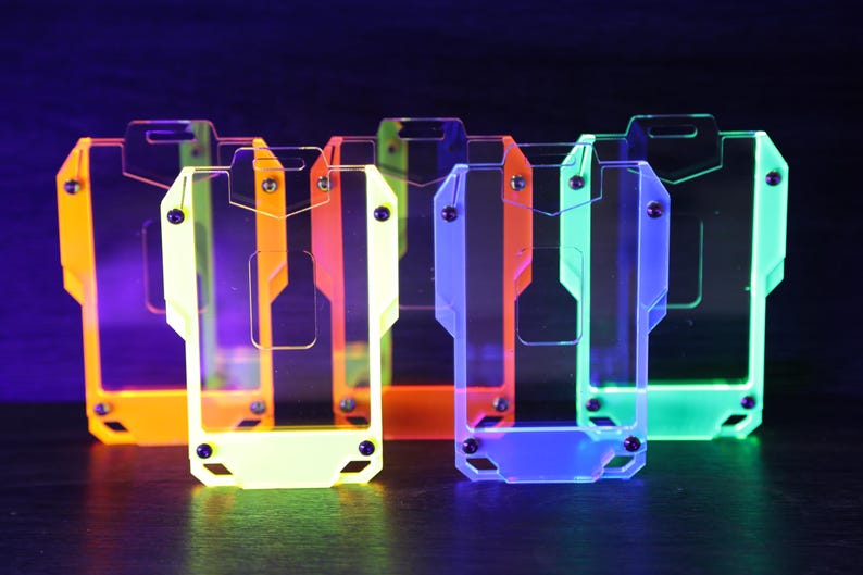 May include: A collection of five rectangular badge holders made of translucent acrylic in neon orange, yellow, red, blue, and green. Each holder features a central cutout, a top slot for a lanyard, and four small black screws securing the frame.
