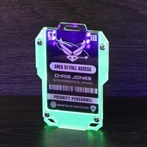 May include: A rectangular acrylic badge with a glowing neon green edge, featuring the text AREA 51 FULL ACCESS, CHRIS JONES, EXTRATERRESTRIAL AFFAIRS, and PRIORITY PERSONNEL. The badge includes a level 9 indicator, a barcode, and a biometric icon.
