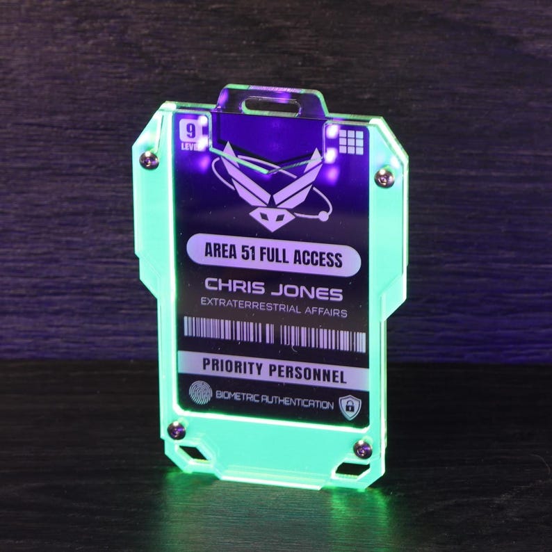 May include: A rectangular acrylic badge with a glowing neon green edge, featuring the text AREA 51 FULL ACCESS, CHRIS JONES, EXTRATERRESTRIAL AFFAIRS, and PRIORITY PERSONNEL. The badge includes a level 9 indicator, a barcode, and a biometric icon.