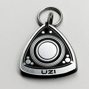 May include: A silver metal keychain shaped like a rotary engine with a black center and the word "UZI" printed on the bottom.