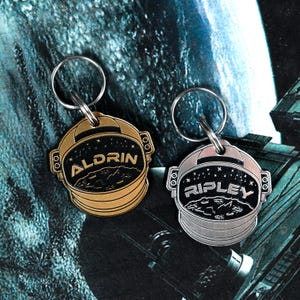 Può includere: Due portachiavi a forma di astronauta, uno dorato e uno argentato. Il portachiavi dorato ha il nome "ALDRIN" e il portachiavi argentato ha il nome "RIPLEY".