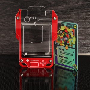 May include: A red and clear acrylic card holder with a retro video game console design. A colorful trading card with a cartoon character is displayed next to the holder. The card features the text "Pika Jab" and "Rocket Thrust".