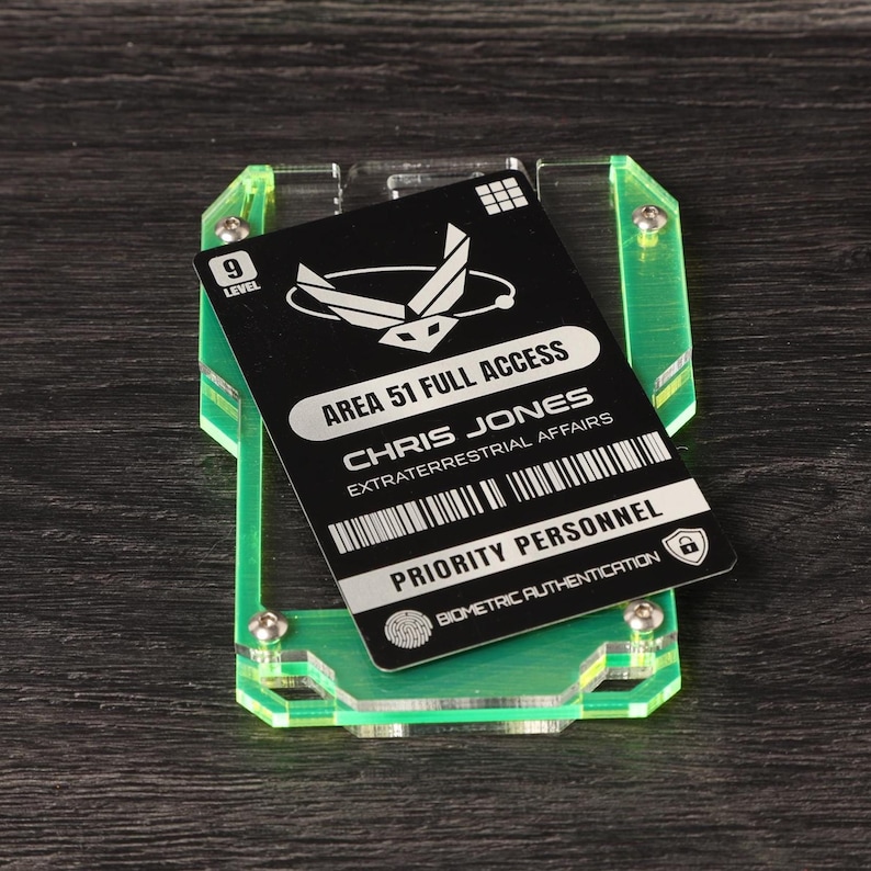 May include: A black rectangular identification card labeled AREA 51 FULL ACCESS CHRIS JONES EXTRATERRESTRIAL AFFAIRS PRIORITY PERSONNEL BIOMETRIC AUTHENTICATION held within a neon green translucent acrylic frame secured by four metal screws.