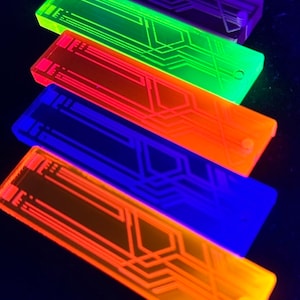 Op de afbeelding: Een verzameling rechthoekige, gloeiende objecten in paars, groen, oranje, blauw en geel. Elk object heeft een printplaatachtig ontwerp op het oppervlak. De objecten zijn diagonaal geplaatst tegen een donkere achtergrond.