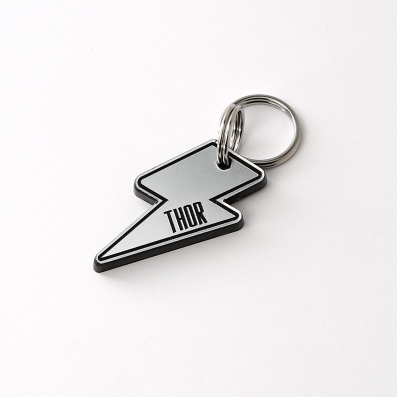May include: Silver lightning bolt shaped dog tag with a black border and the word "THOR" printed in black letters.