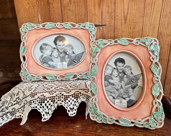 May include: Two oval picture frames with a peach-colored border and green leaf accents. Each frame holds a black and white photo of a family. The frames are displayed on a wooden surface.