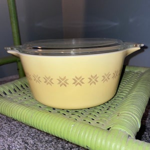 May include: A yellow casserole dish with a glass lid. The dish has a brown geometric pattern around the top.