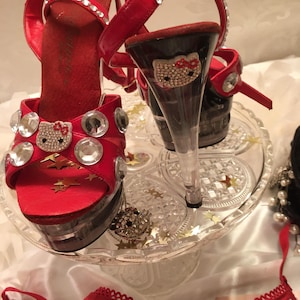 Könnte beinhalten: Rote hochhackige Plateausandalen mit durchsichtigen Absätzen und einem Hello-Kitty-Design auf der Vorderseite des Schuhs. Die Schuhe sind mit Strasssteinen verziert.