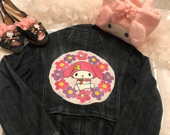 May include: A dark blue denim jacket with a large embroidered patch featuring My Melody, a pink rabbit character, surrounded by colorful flowers. The patch is adorned with rhinestones.