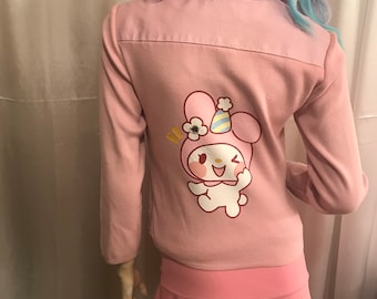 May include: Pink jacket with a white and pink cartoon character wearing a party hat on the back. The character has a flower in its hair and is smiling. The jacket has long sleeves and a zipper closure.