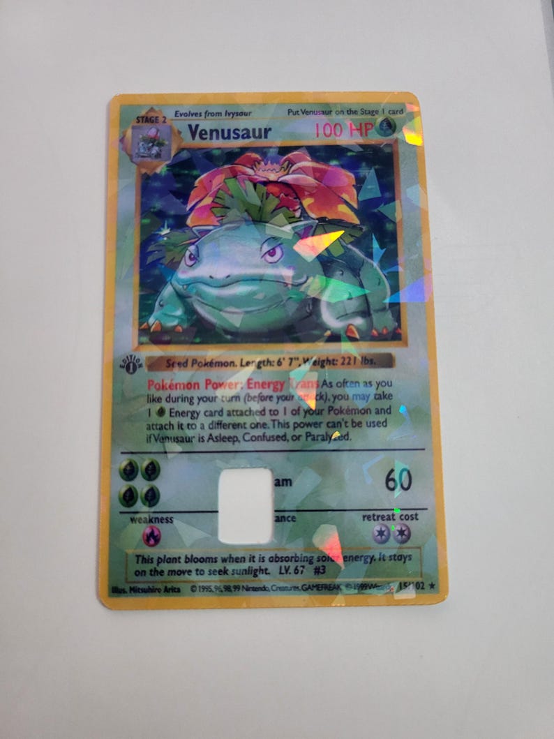 Puede incluir: Una carta hologr&aacute;fica de Venusaur Pok&eacute;mon. La carta presenta un Venusaur verde y azul con una gran flor roja y verde en su espalda. La carta tiene el texto "Venusaur" y "100 HP".