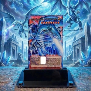 May include: A Yu-Gi-Oh! trading card depicting a blue dragon, displayed on a black stand. The card is set against a fantasy background with dragons, temples, and crystals. The card's text is visible, with measurements in cm.