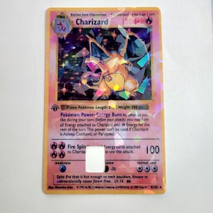 May include: A holographic Charizard Pokémon card. The card features a large orange dragon with wings, flames, and the name "Charizard". The card has text that reads "STAGE 2", "120 HP", and "Fire Spin".