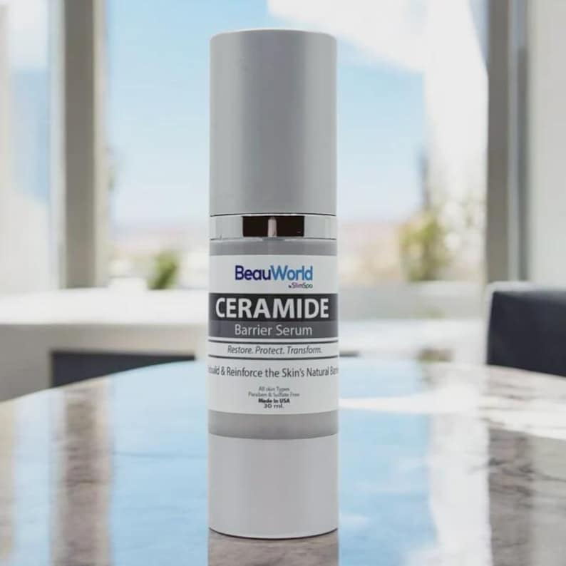 Puede incluir: Un frasco blanco de suero de barrera de ceramida BeauWorld Skin Soo. El frasco tiene una tapa plateada y una etiqueta que dice "Restaurar. Proteger. Transformar. Construir y reforzar la barrera natural de la piel. Todos los tipos de piel. Sin parabenos ni sulfatos. Hecho en EE. UU. 30 ml."