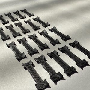 May include: A set of 18 black plastic clips, arranged in rows, with a slight curve to them. The clips are all identical and appear to be made of a durable material.