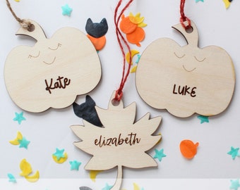 May include: Three wooden ornaments in the shape of a pumpkin and a leaf. The pumpkin ornaments are decorated with a smiling face and the names "Kate" and "Luke". The leaf ornament is decorated with the name "elizabeth".