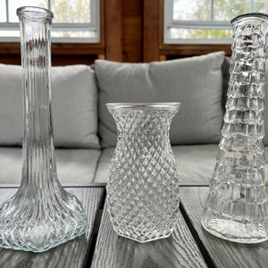May include: Three clear glass vases with different textured patterns. The vases are sitting on a wooden surface.
