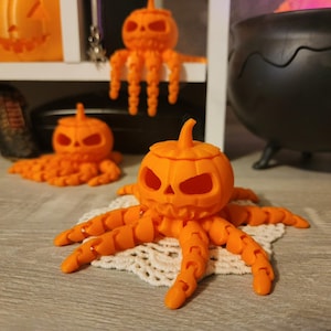 May include: Three orange pumpkin-shaped containers with octopus-like legs. The pumpkins have carved jack-o'-lantern faces. The pumpkins are on a white doily and a wooden surface.