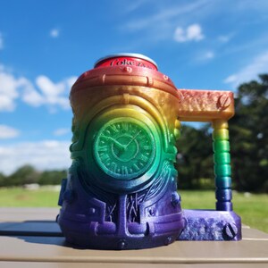 Könnte beinhalten: Ein regenbogenfarbener 3D-gedruckter Dosenhalter mit einem Zifferblatt und einem Griff. Der Halter ist für eine Standarddose mit Soda oder Bier ausgelegt.