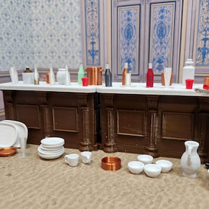 May include: Miniature bar scene with a bartender figure, featuring a brown bar with various bottles, glasses, and cups. White plates, bowls, and a copper-colored pan are in the foreground. A woman in a red dress and black vest stands near the bar.