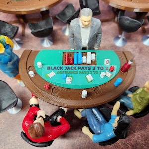 May include: A miniature casino scene featuring a blackjack table with the text "BLACK JACK PAYS 3 TO 2 INSURANCE PAYS 2 TO 1". The scene includes figurines of players, chips, cards, and a dealer, along with miniature chairs and tables.