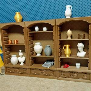 May include: A set of three wooden shelves with various decorative items, including vases, busts, and a typewriter. The shelves are brown with a decorative trim and are arranged in a row against a blue wall.