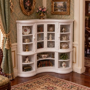 May include: A white corner curio cabinet with glass doors and multiple shelves displaying miniature decorative items, including small porcelain plates, figurines, books, and metallic vessels, arranged within a room setting.