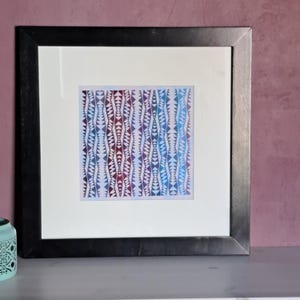 May include: A square framed artwork featuring a repeating vertical pattern of small triangles in shades of blue, purple, and magenta. The print is centered within a wide white mat board and enclosed in a simple, smooth black wooden frame.