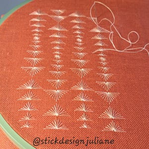 Puede incluir: Un proyecto de bordado sobre tela naranja quemado con cuatro columnas verticales de puntadas blancas en forma de abanico. Una aguja plateada con hilo blanco se sitúa arriba a la derecha. El texto @stickdesignjuliane está abajo.