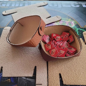 May include: A brown leather pouch with a red and white design, filled with red square game pieces. The pouch is open and the pieces are visible.