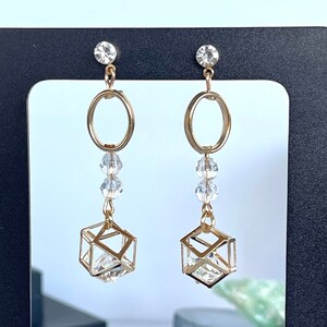 May include: Gold tone earrings with a clear crystal cube and a clear crystal circle dangle. The earrings have a clear crystal stud.