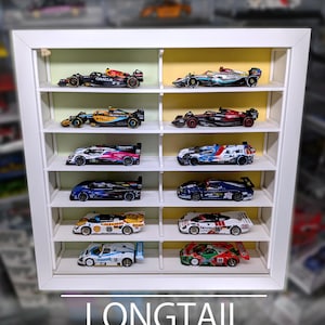 Pu&ograve; includere: Una vetrinetta rettangolare bianca con dodici scomparti individuali, ognuno contenente un'auto da corsa in miniatura. L'unit&agrave; presenta un pannello posteriore interno verde chiaro e giallo. Il testo in basso recita LONGTAIL WHITE 12 SLOTS | LONG CARS | UP TO 90mm.