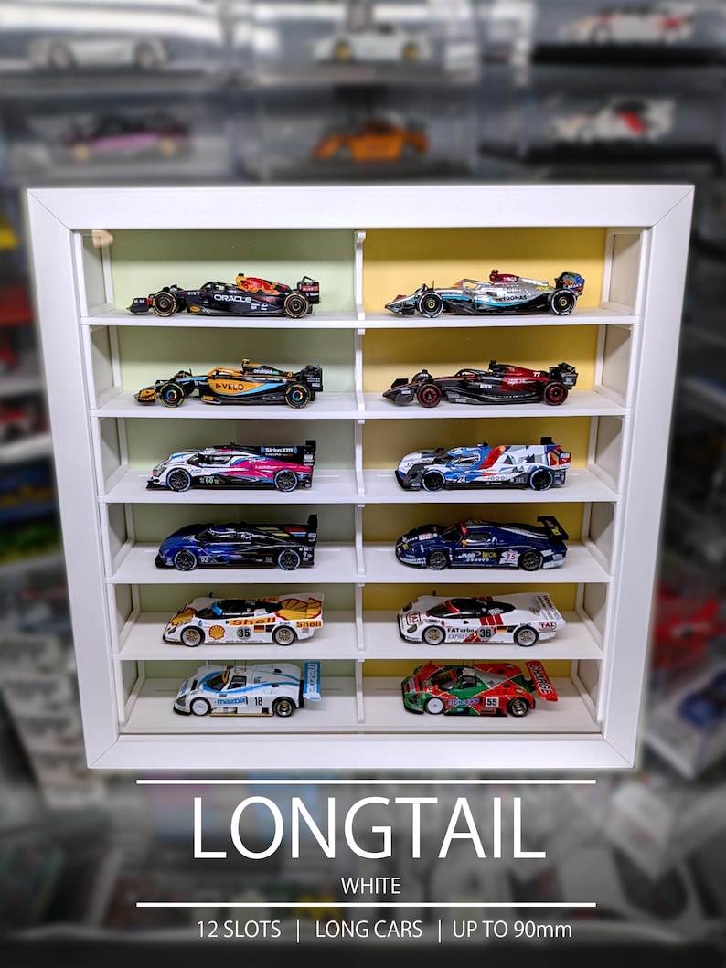 Pu&ograve; includere: Una vetrinetta rettangolare bianca con dodici scomparti individuali, ognuno contenente un'auto da corsa in miniatura. L'unit&agrave; presenta un pannello posteriore interno verde chiaro e giallo. Il testo in basso recita LONGTAIL WHITE 12 SLOTS | LONG CARS | UP TO 90mm.