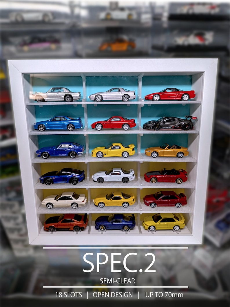 Pu&ograve; includere: Una vetrinetta bianca con 18 scomparti contenente varie macchinine giocattolo in miniatura. L'unit&agrave; presenta un design aperto e un pannello posteriore azzurro e giallo. Il testo in basso recita: SPEC.2, SEMI-CLEAR, 18 SLOTS | OPEN DESIGN | UP TO 70mm.