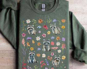 May include: A green sweatshirt with a print of raccoons and flowers. The raccoons are in various poses, and the flowers are in a variety of colors.