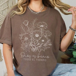 May include: A brown t-shirt with a white floral design and the text "Dios es bueno todo el tiempo".