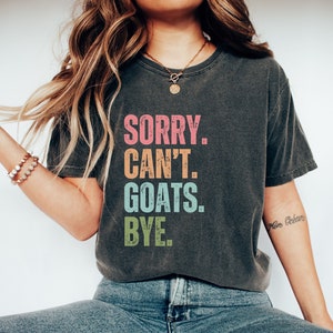 May include: A dark gray t-shirt with the text "SORRY. CAN'T. GOATS. BYE." printed in colorful letters.