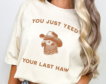 May include: A white t-shirt with the text "You just yeed your last haw" in brown text. A cartoon parrot wearing a cowboy hat is above the text.