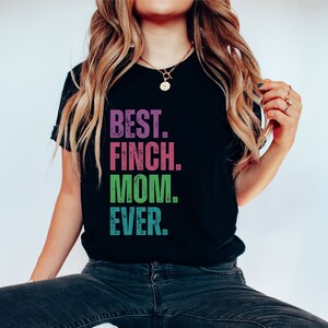 May include: A black t-shirt with the text "BEST. FINCH. MOM. EVER." in colourful, distressed lettering.