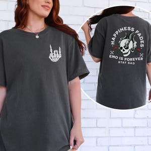 May include: Dark grey t-shirt with a white skeleton hand graphic on the front. The back of the shirt features a skull with flames, roses, and the text "HAPPINESS FADES. EMO IS FOREVER STAY SAD."