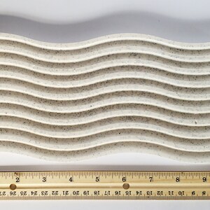 May include: A white, speckled, wavy silicone baking mat measuring 12 inches long. The mat has 10 raised, wavy lines.